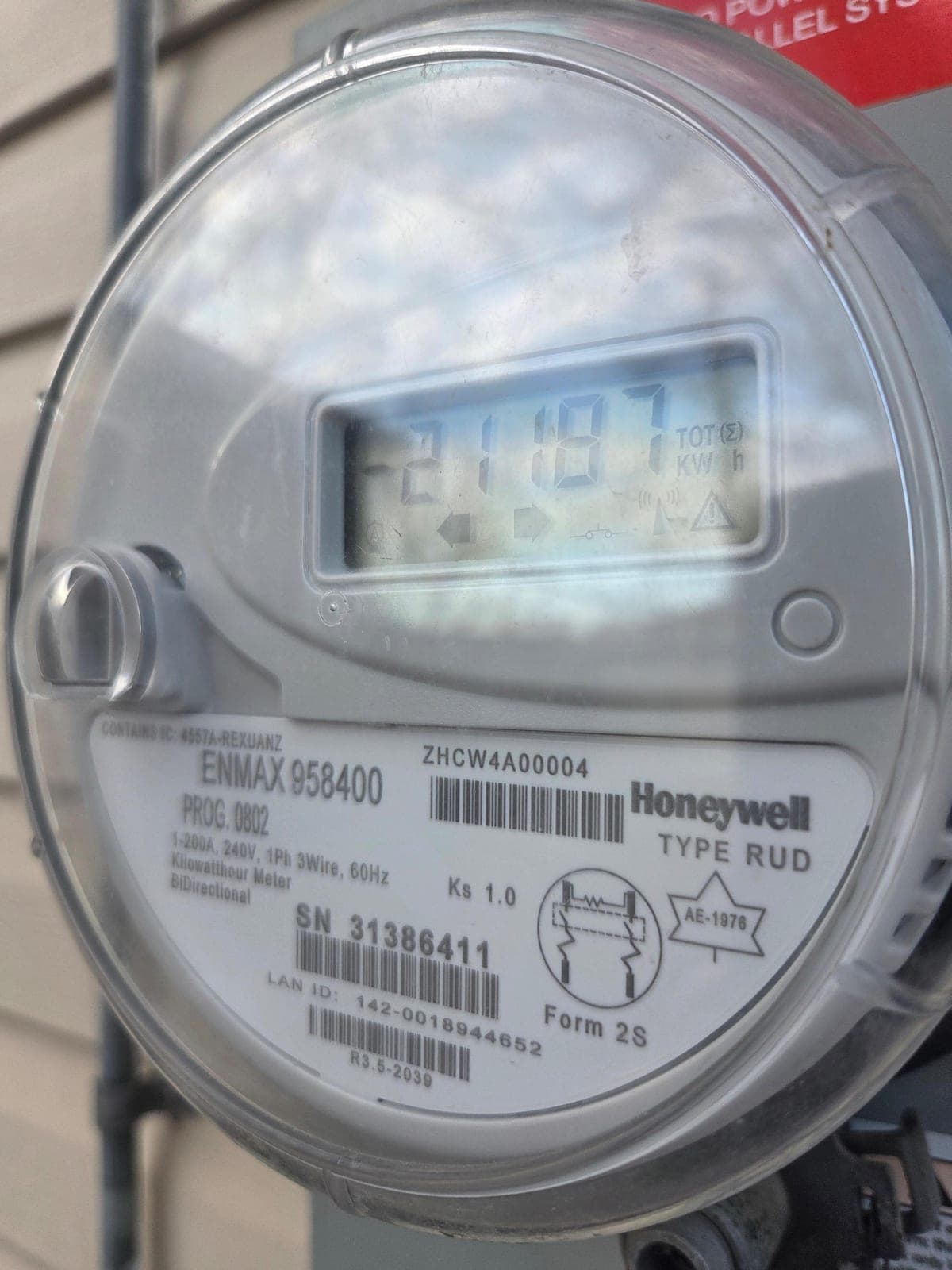 Same ENMAX bi-directional meter a few seconds later showing 21187 TOT (Sigma) kWh with the left-pointing arrow lit, indicating cumulative kilowatt-hours delivered from the home to the grid.
