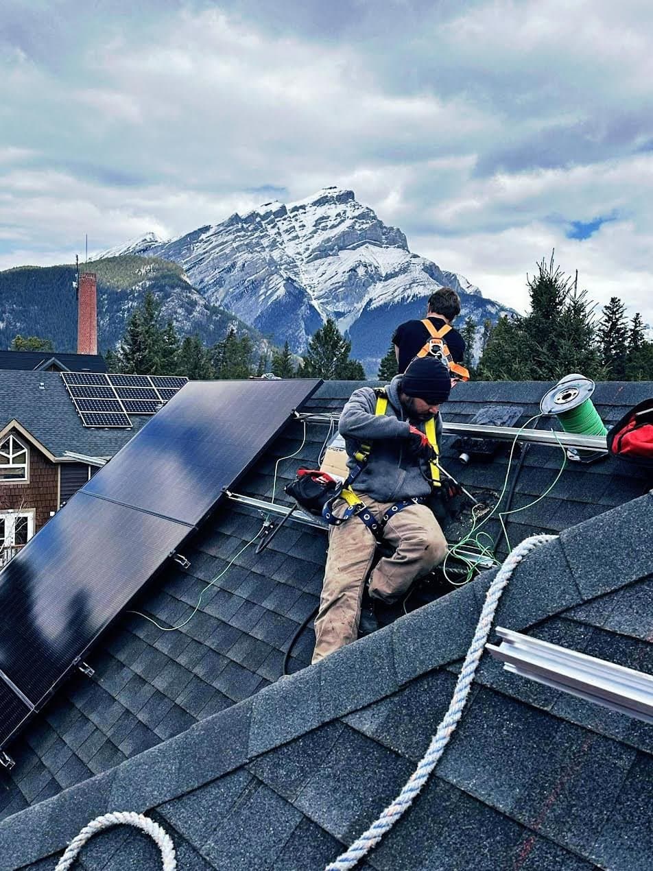 Flux Renewables crew installing solar panels on a Banff roof with Cascade Mountain behind