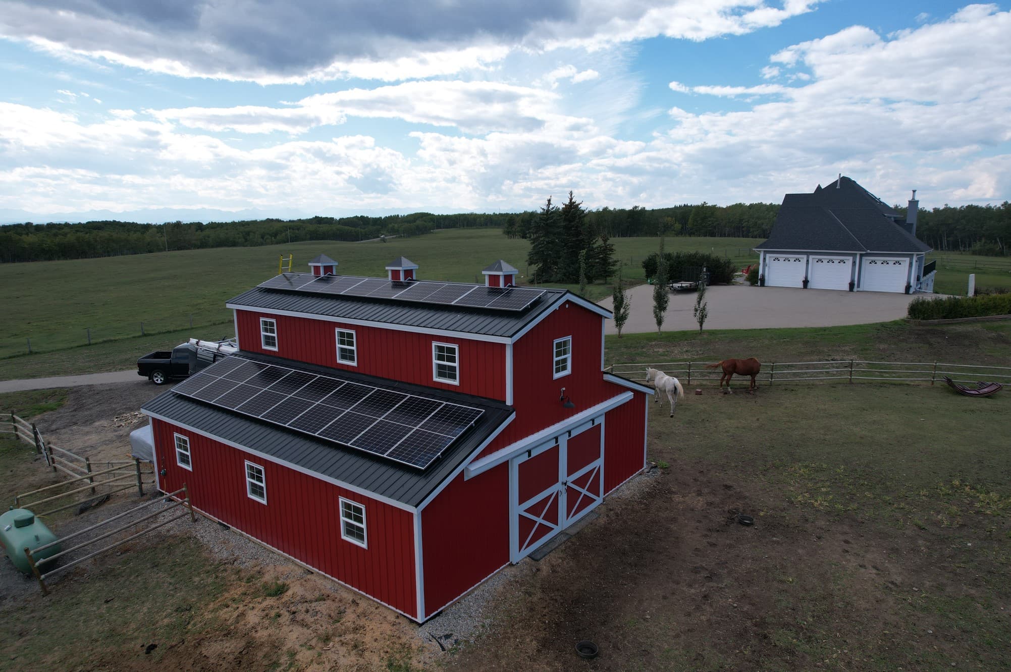 Red barn near Calgary with a Flux Renewables solar array on the roof, horses grazing in the foreground